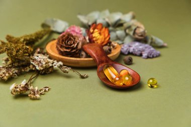 Alternatif ve bitkisel ilaçlar, taze mandalina yaprakları, ahşap kaşıkta yağ ve vitamin içeren kapsüller, kuru kokulu çiçekler ve şifalı bitkiler, yeşil arka plandaki hastalıkların tedavisi için iyi bir sağlık.