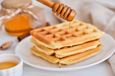 Taze Belçika waffle 'larının üzerine bal dökülüyor. Mineral ve vitamin açısından zengin organik sağlıklı kahvaltı. Kahvaltı için eko-yemek. Moda tatlı şekerlemeler