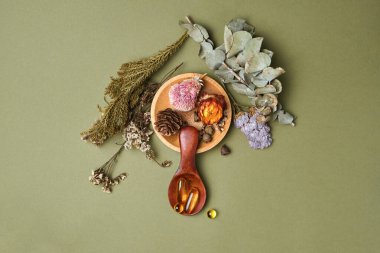 Alternatif ve bitkisel ilaçlar, taze mandalina yaprakları, ahşap kaşıkta yağ ve vitamin içeren kapsüller, kuru kokulu çiçekler ve şifalı bitkiler, yeşil arka plandaki hastalıkların tedavisi için iyi bir sağlık.