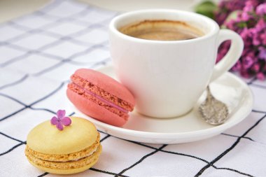 Bir fincan kahve ve lezzetli kurabiyelerden yakın çekim. Beyaz kareli masa örtüsü üzerinde makarna ve kahve Americano.