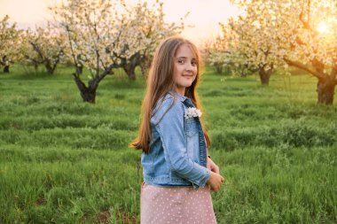 Küçük mutlu kız çiçek açan bahçedeki beyaz çiçeklerle çiçek açan elma ağaçlarının altında oynuyor. Çocuklar için bahar eğlencesi güzel bir bahar bahçesinde.