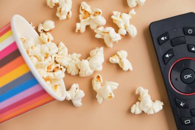 Bir kova patlamış mısır, bej arka planda televizyon kumandası. Boş zaman ve eğlence konsepti. Üst görünüm