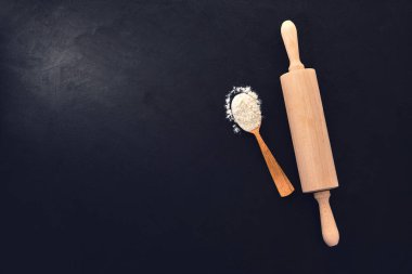 Tahta kaşıkta buğday unu. Tasarımın için fırın arka planında merdane var. Siyah bir arkaplanda. Üst görünüm, seçici odak