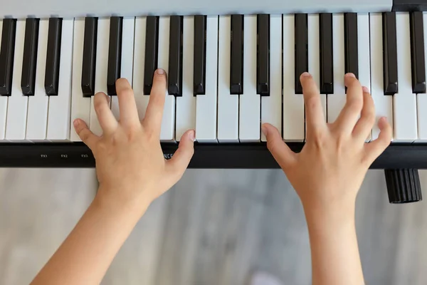 Selective focus of kid\'s fingers playing the piano. There are musical instrument for concert or learning music. Close up hand of child musician playing the piano, top view