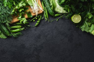 Taze sebzeler ve siyah desenli arka planda ahşap kesim tahtası. lahana, kabak, salatalık, nane, limon, ıspanak, soğan ve diğerleri. Üst Manzara. Metnin için boş yer.