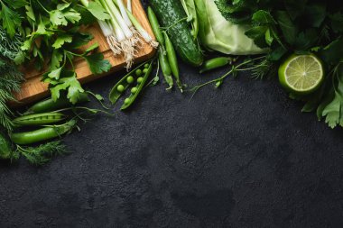 Yeşil taze sebzeler ve siyah desenli arka planda fotokopi alanı olan ahşap kesme tahtası. lahana, kabak, salatalık, nane, limon, ıspanak, soğan ve diğerleri. Üst Manzara. Metnin için boş yer.