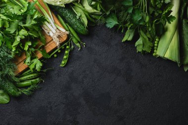 Yeşil taze sebzeler ve siyah desenli arka planda fotokopi alanı olan ahşap kesme tahtası. lahana, kabak, salatalık, nane, limon, ıspanak, soğan ve diğerleri. Üst Manzara. Metnin için boş yer.