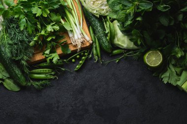 Taze sebzeler ve siyah desenli arka planda ahşap kesim tahtası. lahana, kabak, salatalık, nane, limon, ıspanak, soğan ve diğerleri. Üst Manzara. Metnin için boş yer.