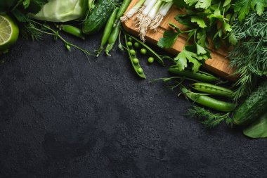 Yeşil taze sebzeler ve siyah desenli arka planda fotokopi alanı olan ahşap kesme tahtası. lahana, kabak, salatalık, nane, limon, ıspanak, soğan ve diğerleri. Üst Manzara. Metnin için boş yer.