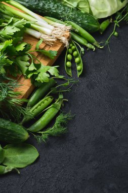 Taze sebzeler ve siyah desenli arka planda ahşap kesim tahtası. lahana, kabak, salatalık, nane, limon, ıspanak, soğan ve diğerleri. Dikey, Üst Manzara. Metnin için boş yer.