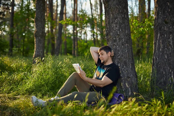 Bel Giovanotto Seduto Nella Foresta Sull Erba Appoggiato Albero Leggere — Foto Stock