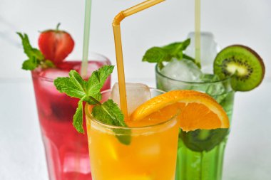 Üç parlak renkli lezzetli soğuk limonata sürahisi kivi, portakal ve çilek karışımı, açık arkaplanda naneli, kapat.