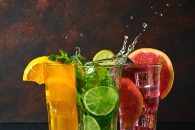 Koyu arkaplan üzerine su sıçratan taştan siyah masada üç klasik kokteyl bardağı. Taze Renkli Meyve Suyu Yeşil Meyve Smoothie Kivili Turuncu Greyfurt Limonlu Kivi Kırmızısı