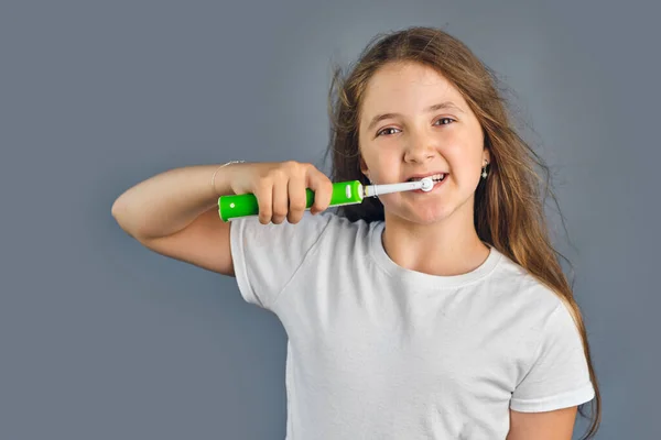 可愛いです子供の女の子とともに彼女の髪ダウン立ってブラッシング彼女の歯とともに電動歯ブラシ 隔離された灰色の背景 — ストック写真