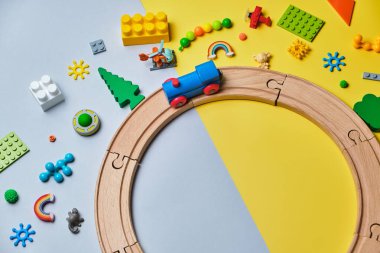 Farklı çocuk oyuncakları seti, ahşap raylardan, trenden, sarı ve mavi arka plandaki yapıcıdan yapılmış yuvarlak metin için fotokopi alanı. Üst manzara, düz uzanma.