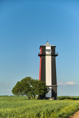 Beautiful landscape with Black and white lighthouse in a wheat green field and a lonely tree against a blue sky in Ukraine