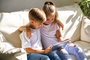 aile, çocuklar, teknoloji ve ev konsepti. Oturma odasındaki kanepede tablet bilgisayarlı gülümseyen kardeşler.