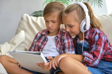 Evde tabletin tadını çıkaran kulaklıklı şirin erkek ve kız kardeşleri var. aile, çocuklar, teknoloji ve ev kavramı