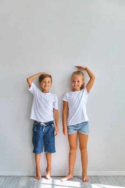 クールな子供たち 小さな男の子と女の子は彼らの高さを測定し 比較し 白い壁の近くに楽しみを持っている — ストック写真