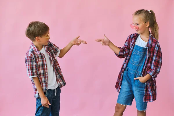 かわいいですスタイリッシュな女の子と男の子で色のサングラスを身に着けています再生シャツに立ってピンクの背景 — ストック写真