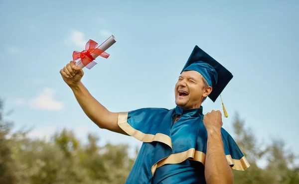 A young happy smiling man celebrates his degree and phd diploma over blue sky. celebrating graduation concept