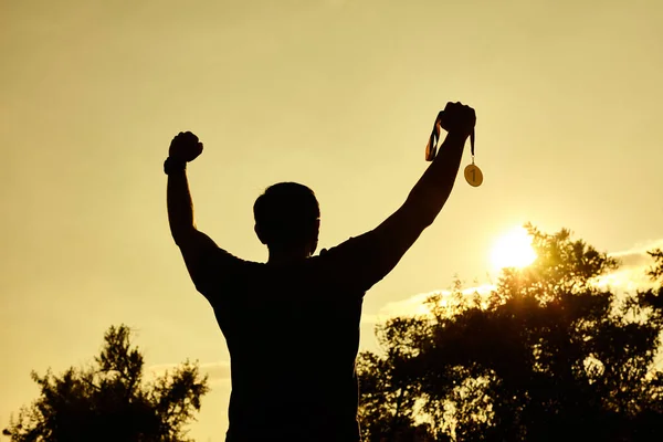 Silhouette man raising hands and holding gold medal with sunset sky. Motivation and success concept.