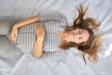 Mutlu hamile anne karnına sevgiyle dokunuyor ve evde yatağa uzanıyor. Hamilelik, annelik, üst düzey sağlık konsepti.