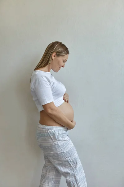 Mooie Zwangere Vrouw Pyjama Staat Tegen Achtergrond Van Een Witte — Stockfoto