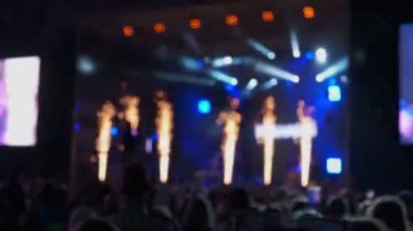 Bulanık görüntüler, açık havada büyük ekranlar ve renkli ışıklarla bir konserde parti yapan bir kalabalığın dikkatini dağıtıyor.