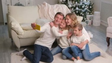 Noel, tatiller, teknoloji ve insanlar konsepti - mutlu aile oturma odasında oturuyor ve akıllı telefonuyla selfie çekiyor.
