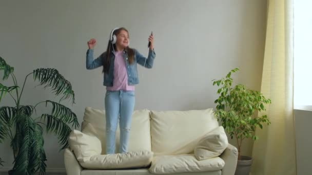 Funny Happy Little Girl Mit Kopfhörern Hüpfen Auf Der Couch — Stockvideo