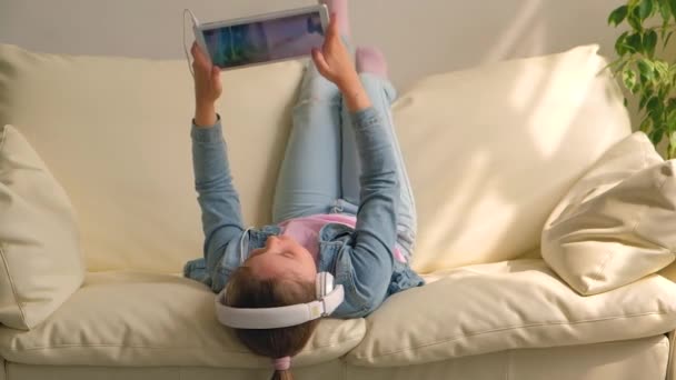 Little Girl Lying Upside Sofa Playing Game Tablet — Stock Video
