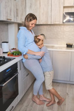 Hamile anne ve çocuk birlikte oynuyorlar ve mutfakta birbirlerine sarılıyorlar. Anne ve oğlu evde kahvaltı ederken iyi duygular paylaşıyorlar..