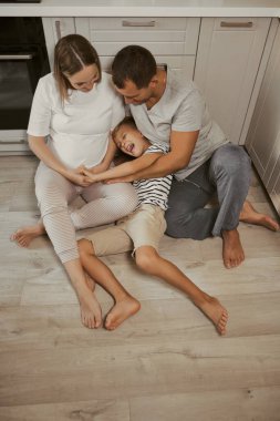 Neşeli bir aile, hamile bir kadın, yerde oturuyor, sarılıyor, eğleniyor, birlikte vakit geçiriyorlar..