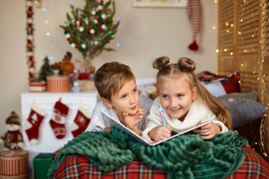 Mutlu Noeller ve mutlu tatiller. Küçük şirin çocuklar Noel Baba 'ya mektup yazıyorlar. Evin içinde Noel ağacının yanında..