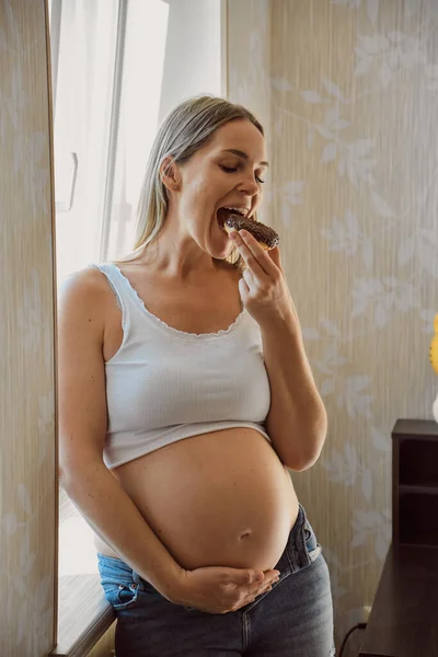 Embarazo Nutrición Mujer Embarazada Disfrutando Donut Cerca Ventana Casa Concepto — Foto de Stock