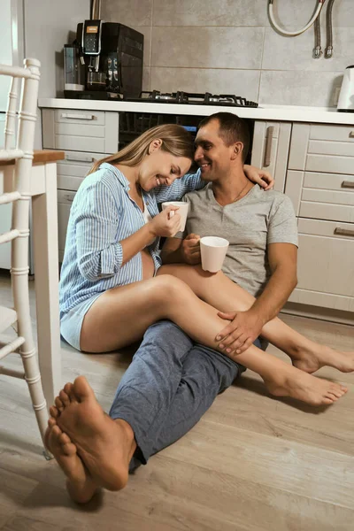 Young Pregnant Couple Kitchen Floor Hug Laugh Cups Tea Rejoicing — Stock Photo, Image