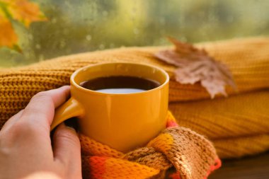 Sarı fincanlı kadın eli eşarplı, arka planda parlak yapraklı. Sonbahar temalı güzel bir fotoğraf..