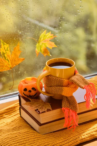 Hello October. Background with books, cup of tea, pumpkin, leaves on the windowsill, it is raining outside the window