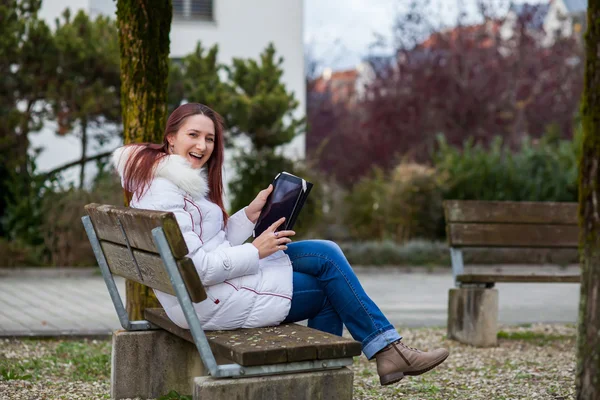 Jovem mulher sentada em um banco de parque com um tablet — Fotografia de Stock