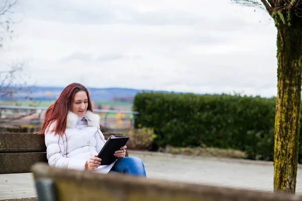 Young woman sitting on a park bench with a tablet — Stock Photo, Image