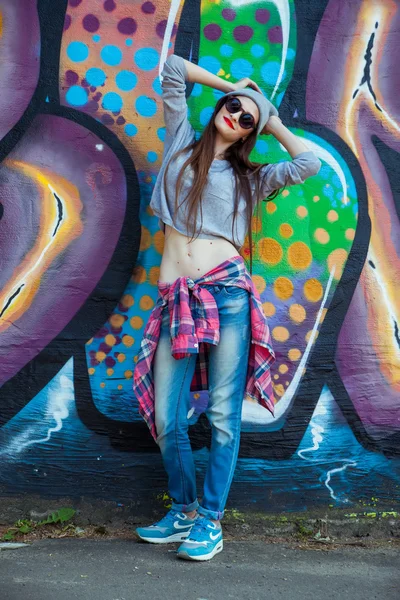 Bela menina legal em chapéu e óculos de sol sobre a parede de grafite — Fotografia de Stock