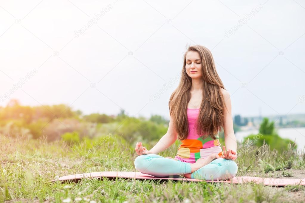 Pretty woman doing yoga exercises on nature landscape