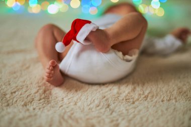 Bir tanesinin ayak parmaklarında minyatür kırmızı bir Noel Baba şapkası olan küçük ayakları havada sırt üstü yatan yeni doğmuş bir bebeğin yakın plan fotoğrafı..