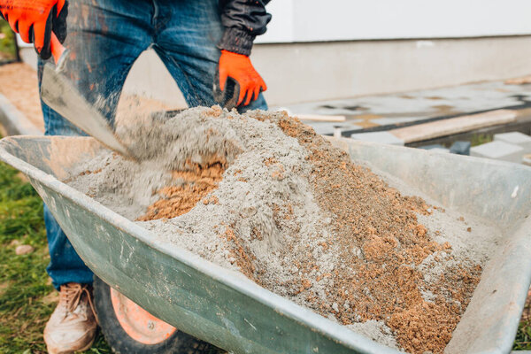 Строитель готовит смесительно-песчаный раствор для укладки тротуарных плит - строительная тачка для работы