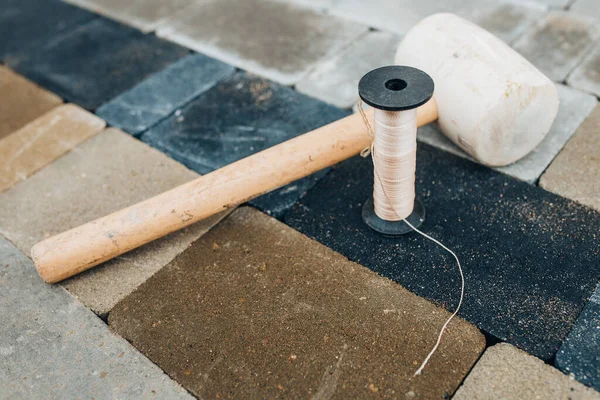 A straight line chopping cord and a rubber mallet with a wooden handle are a bricklayer tools for laying paving slabs