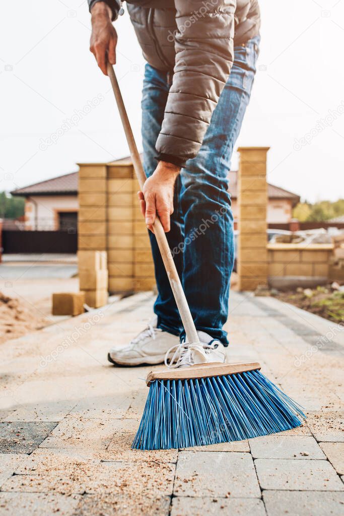 A man tiler fills the seams of paving slabs with sifted sand with a brush - laying paving slabs