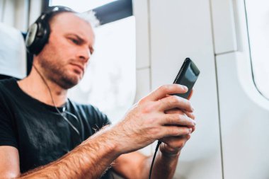 Trendeki beyaz adam akıllı telefondan kulaklıkla müzik dinliyor.