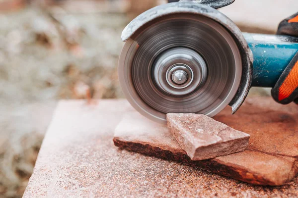 A diamond blade cuts a stone with dust - an electric grinder in the hands of a bricklayer