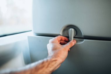 Bir adam ön koltuğun arkasından katlanan bir masayı indirir. Uçak, otobüs ya da trenin yolcu bölümünde yemek yemek ve çalışmak için elverişlidir.